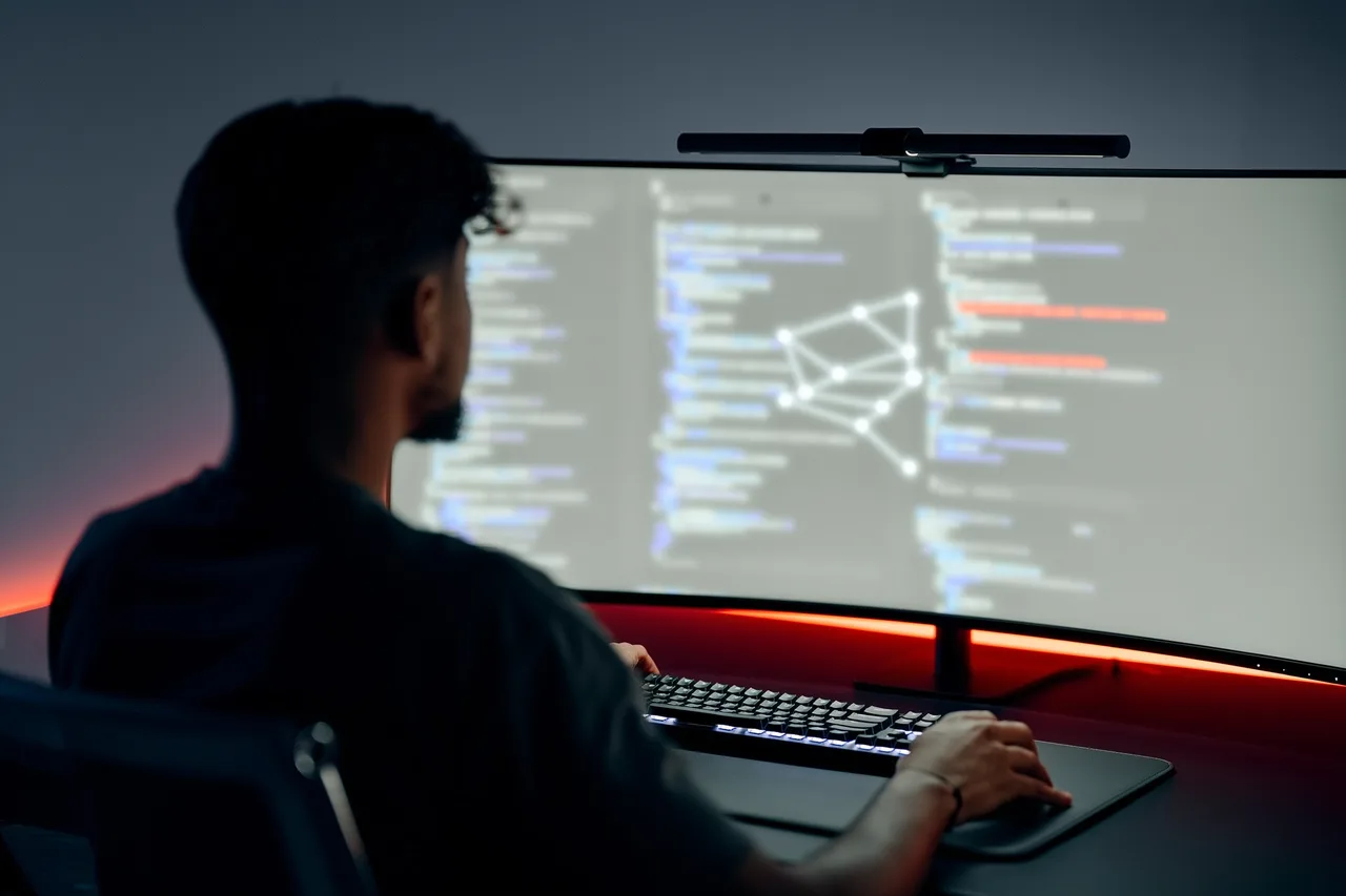 Entwickler vor einem großen Monitor mit unscharfem Code und einem Netzwerkgraphen, rotes Akzentlicht